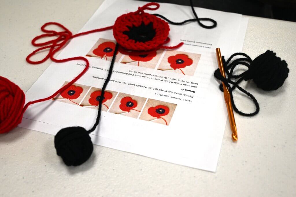 A crochet poppy is on a table with black and red yarn