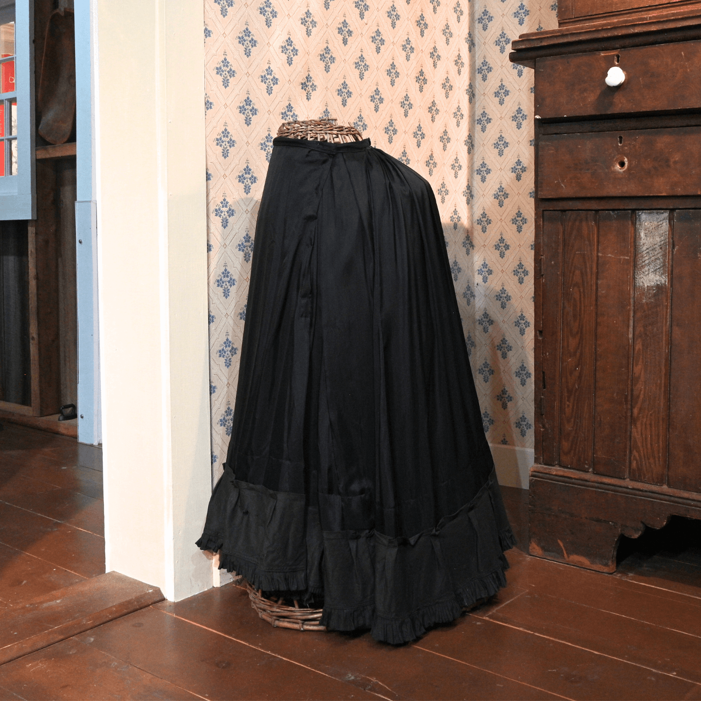 A long black silk shirt rests on a wicker dress form.