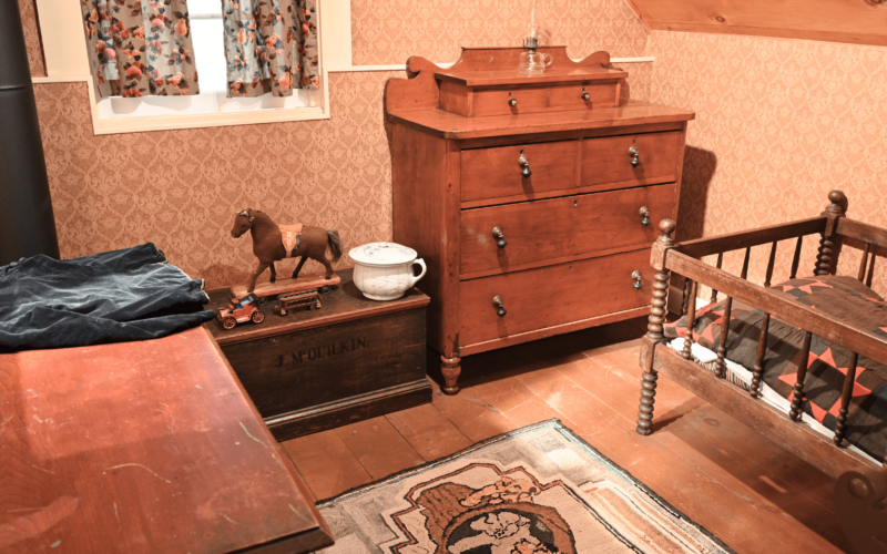 A bedroom with orange wallpaper, wood floors, a small child's bed in the corner and some toys.