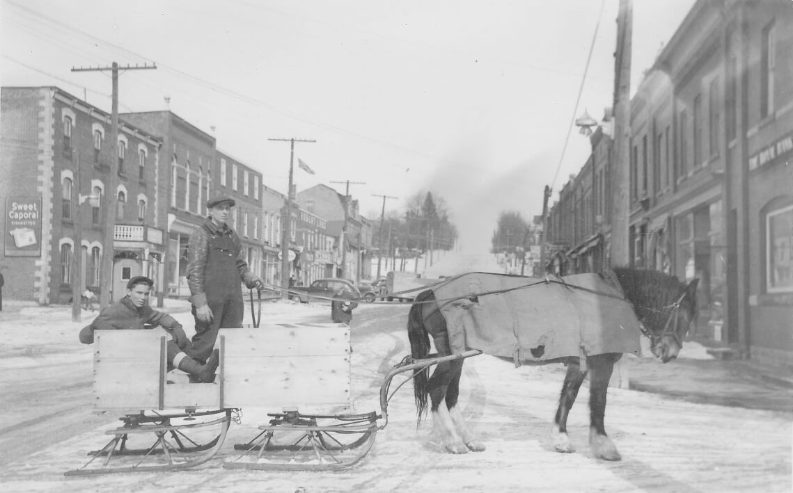 Wilbert Stuckey and Roy Stuckey (seated in sleigh), intersection of Mill and Main Street (looking north), Grand Valley, 1942. MoD Collection